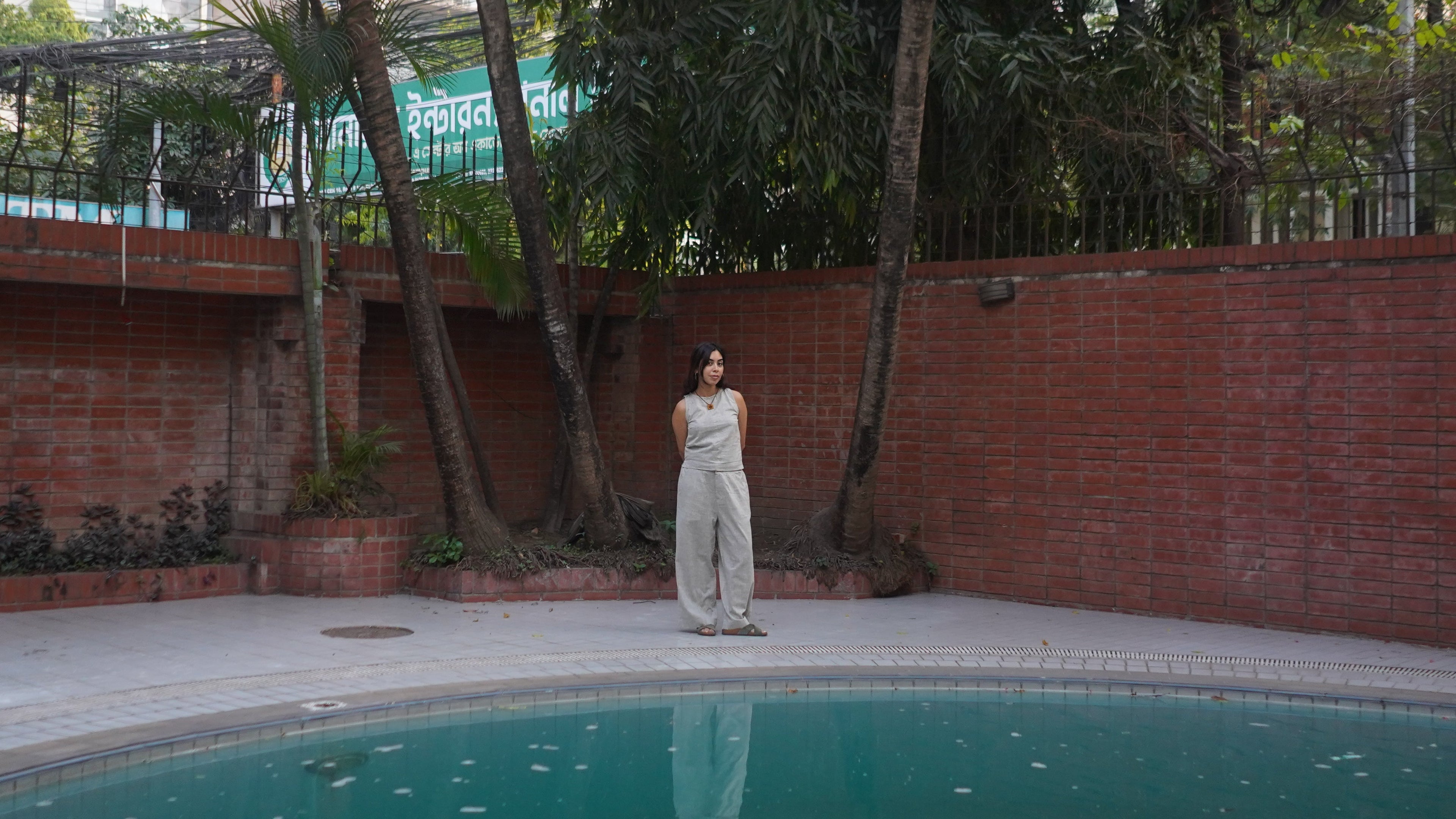 Person standing by a pool with trees and a building in the background